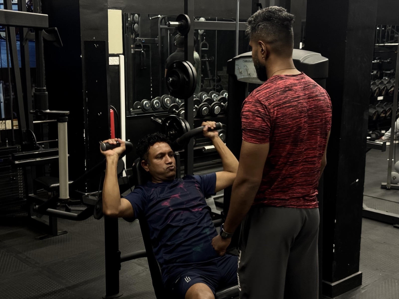 A trainer watching a member press on a plate-loaded machine