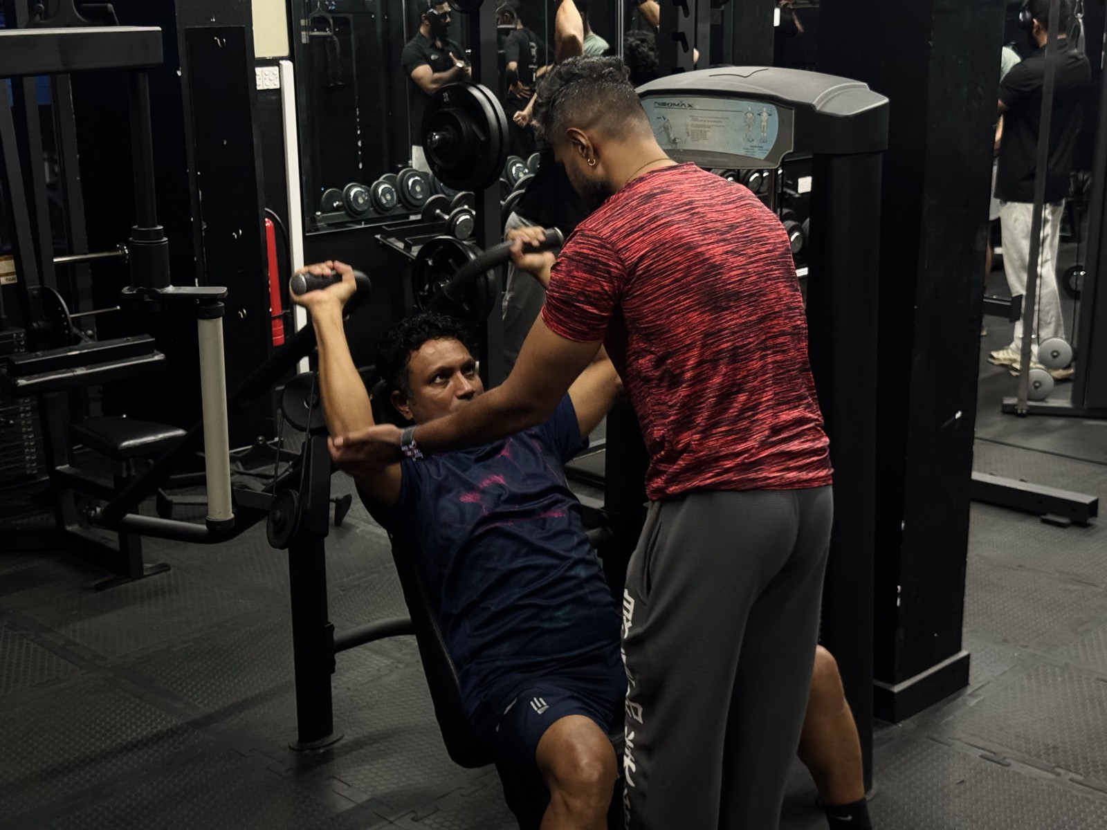 A trainer counting reps beside a seated press machine