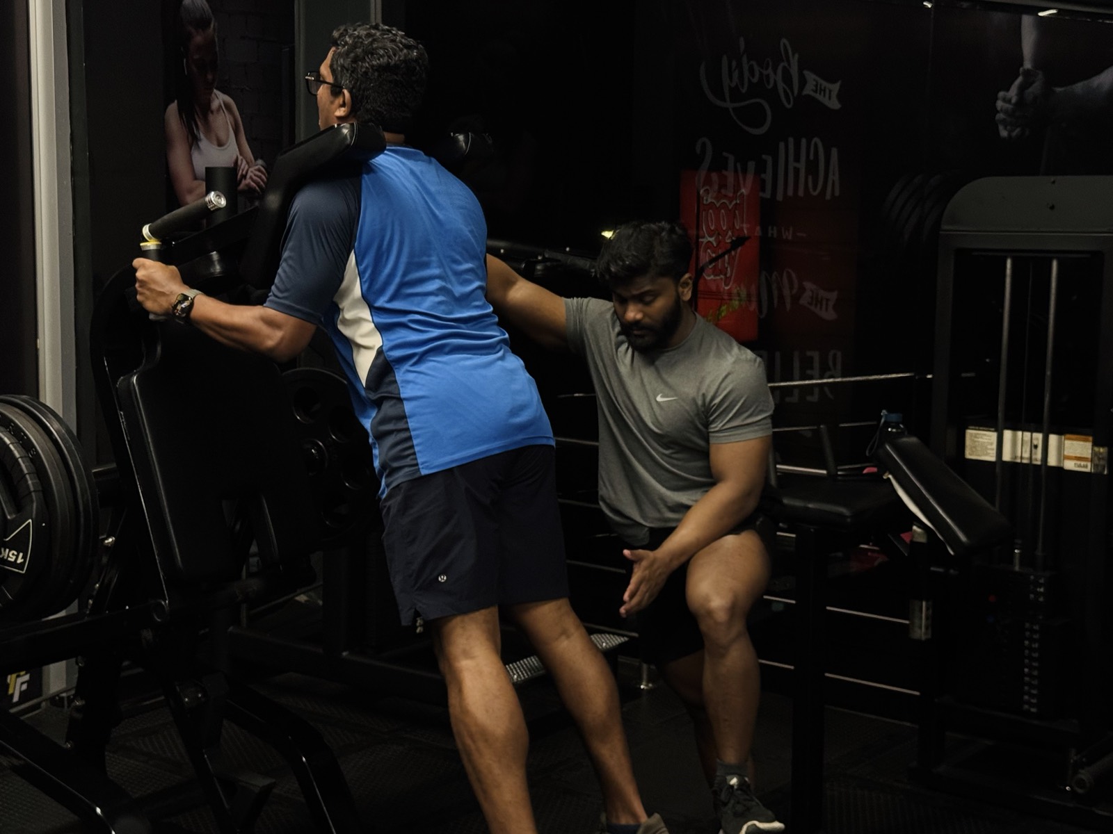 A coach spotting a member mid-set in the strength zone