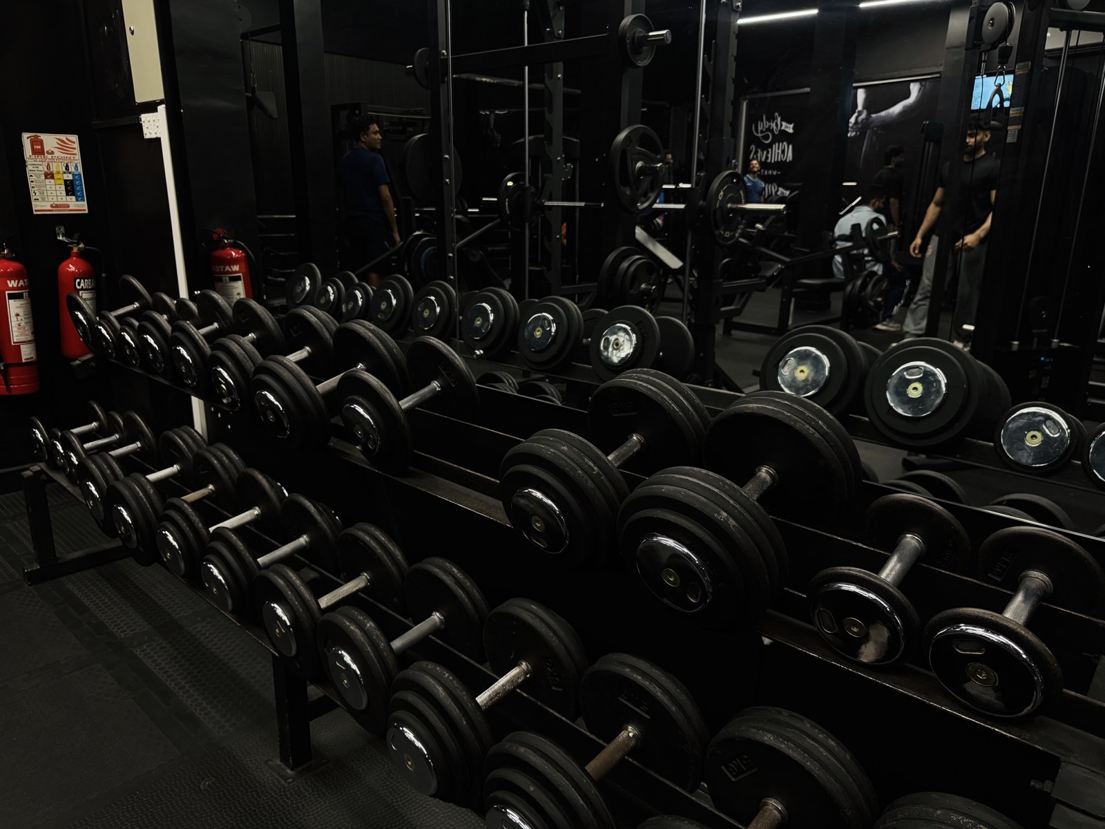 Rows of dumbbells and loaded barbells along the mirrored wall